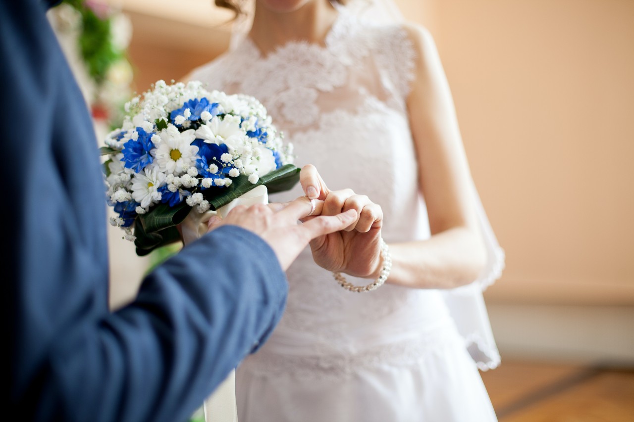 A bride putting the wedding band onto her husband’s finger during the ceremony