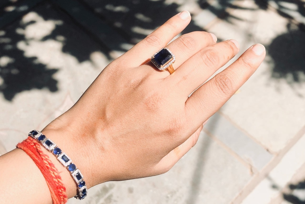 A woman’s wrist shows off a sapphire tennis bracelet, an orange string bracelet, and a black diamond fashion ring.