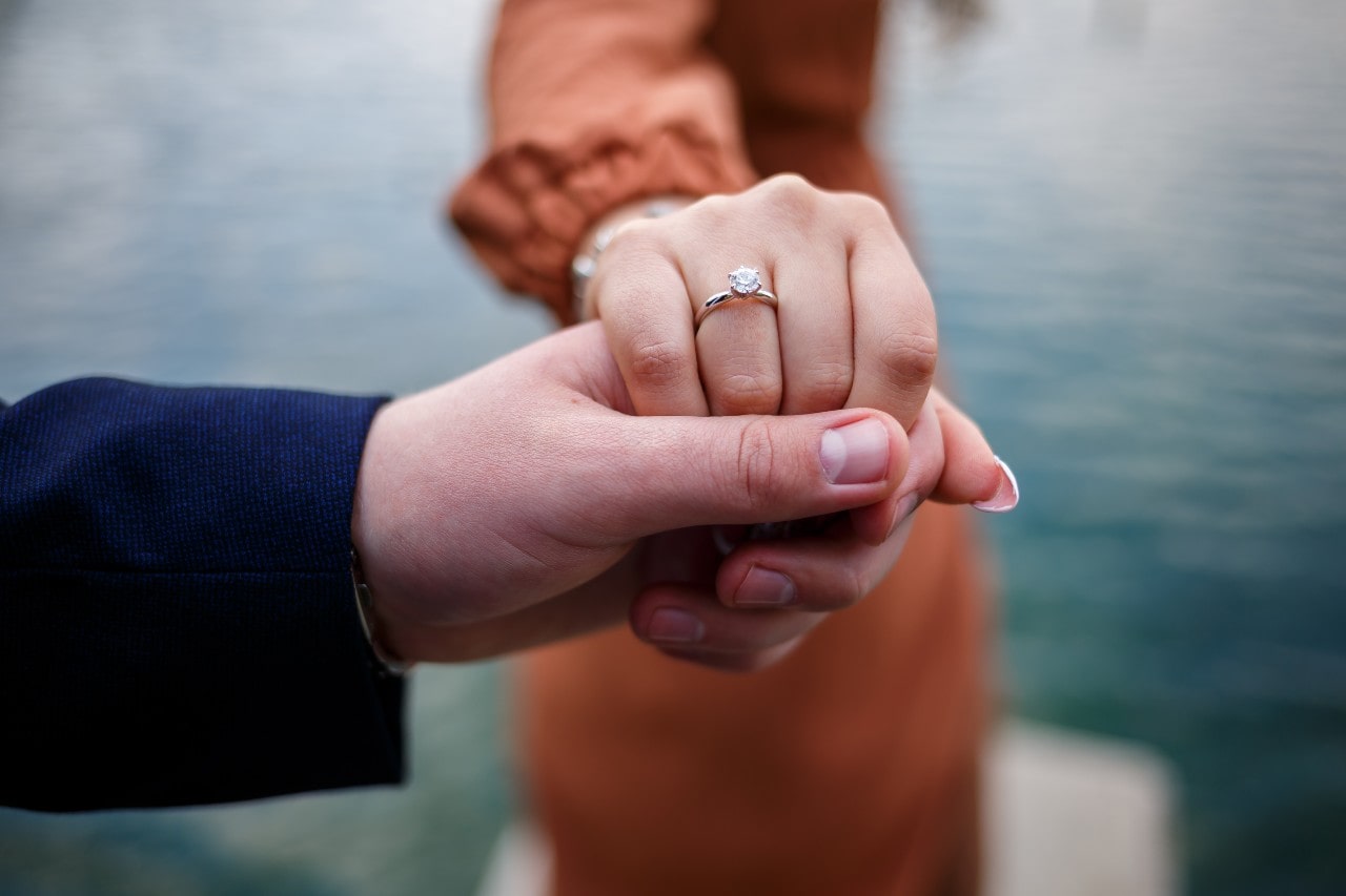 A woman holds hands with her fiance, showing off her white gold solitaire engagement ring.