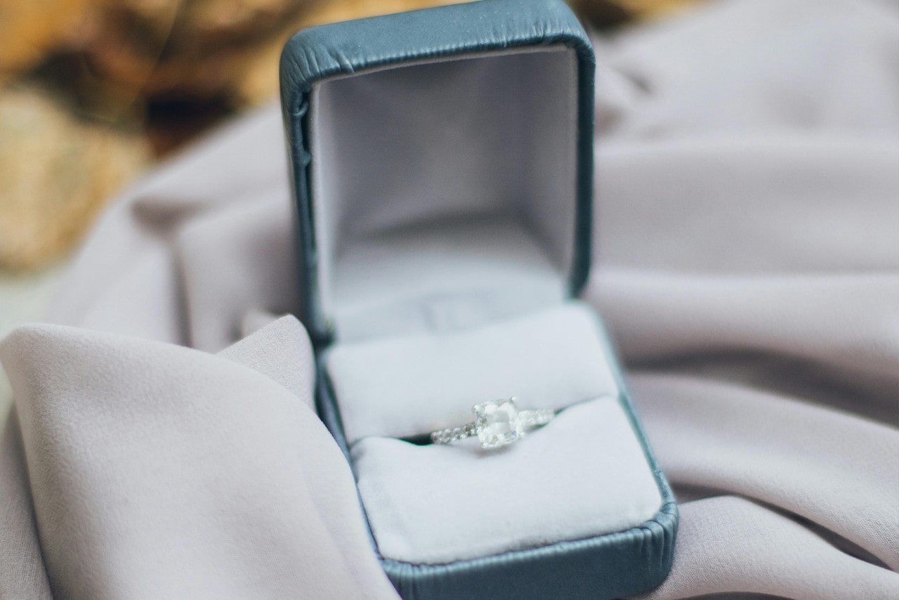 A white gold diamond sidestone engagement rings in a mint green velvet box on top of white fabric