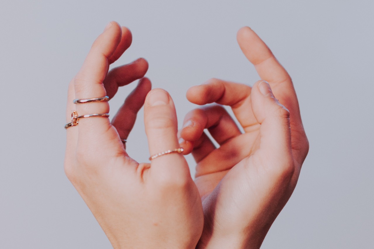 a pair of hands wearing stacked, minimalist gold rings
