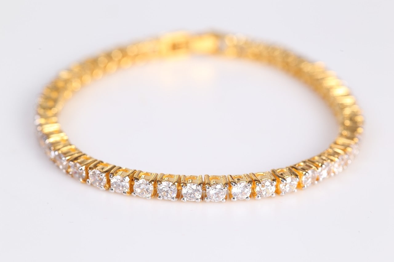 a yellow gold diamond tennis bracelet on a white surface
