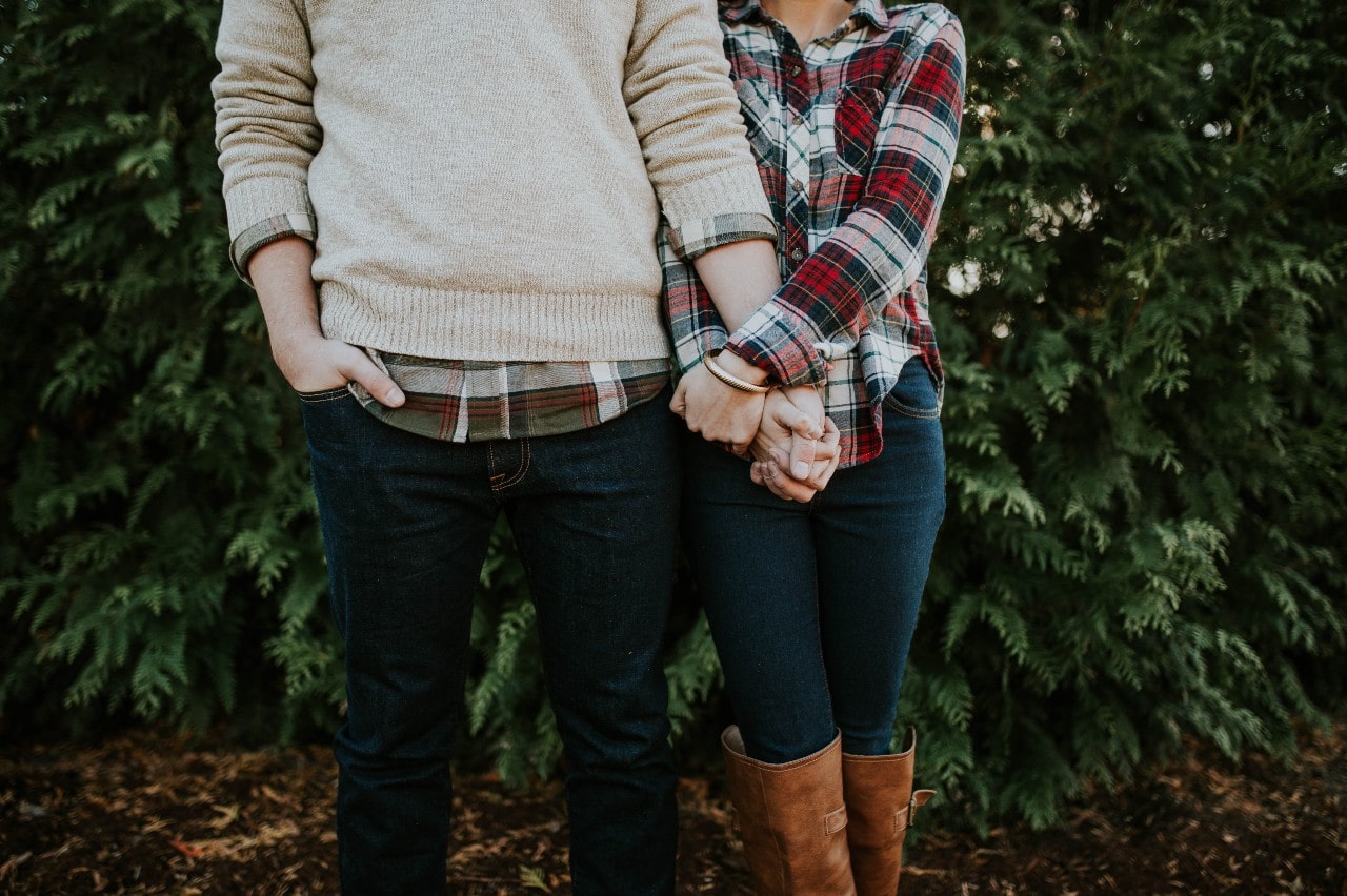 An engaged couple holds hands and poses for a photo during a walk.