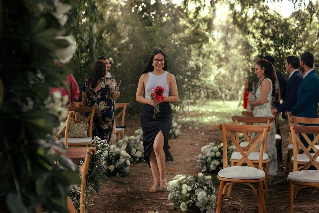 A bridesmaid walking down a fall forest wedding aisle with guests standing from their seats