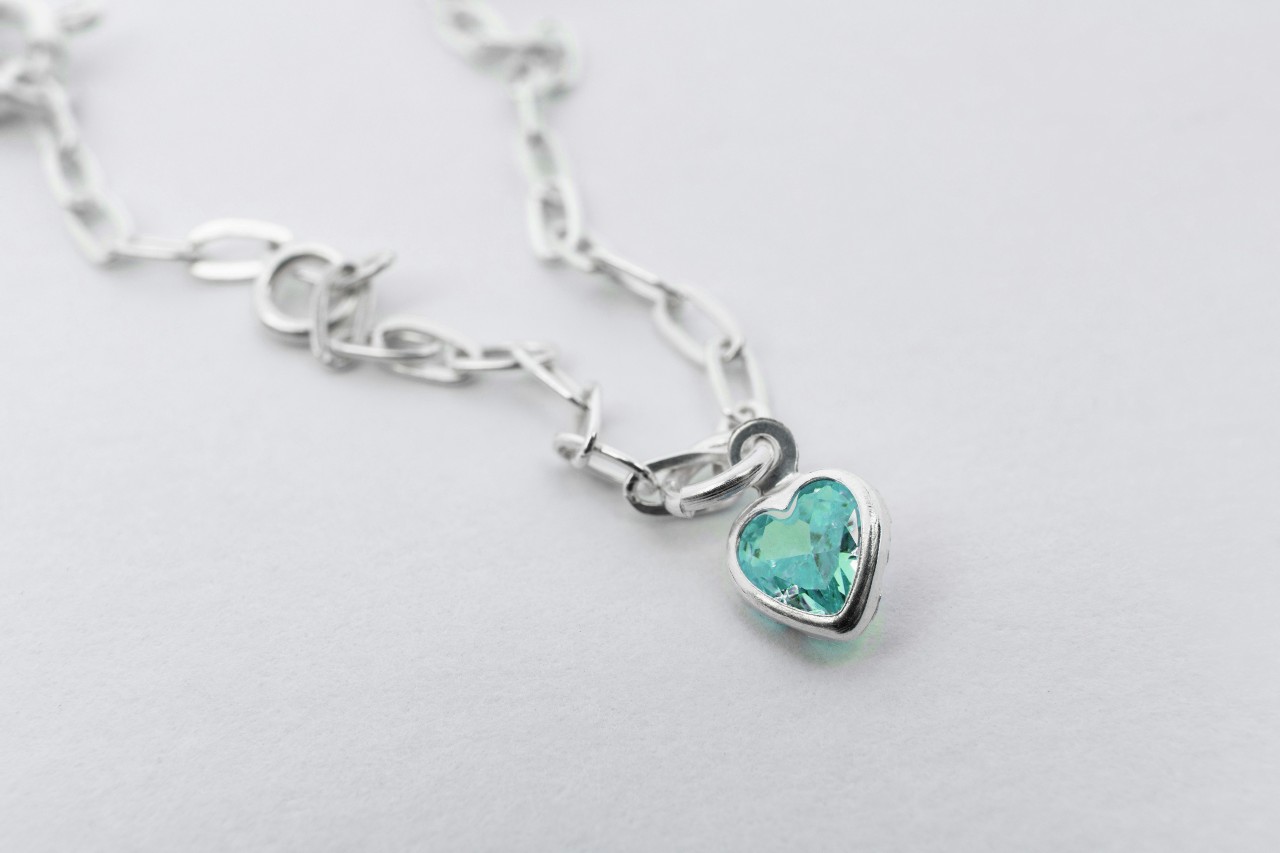 a white gold chain necklace with a heart pendant featuring a blue gemstone