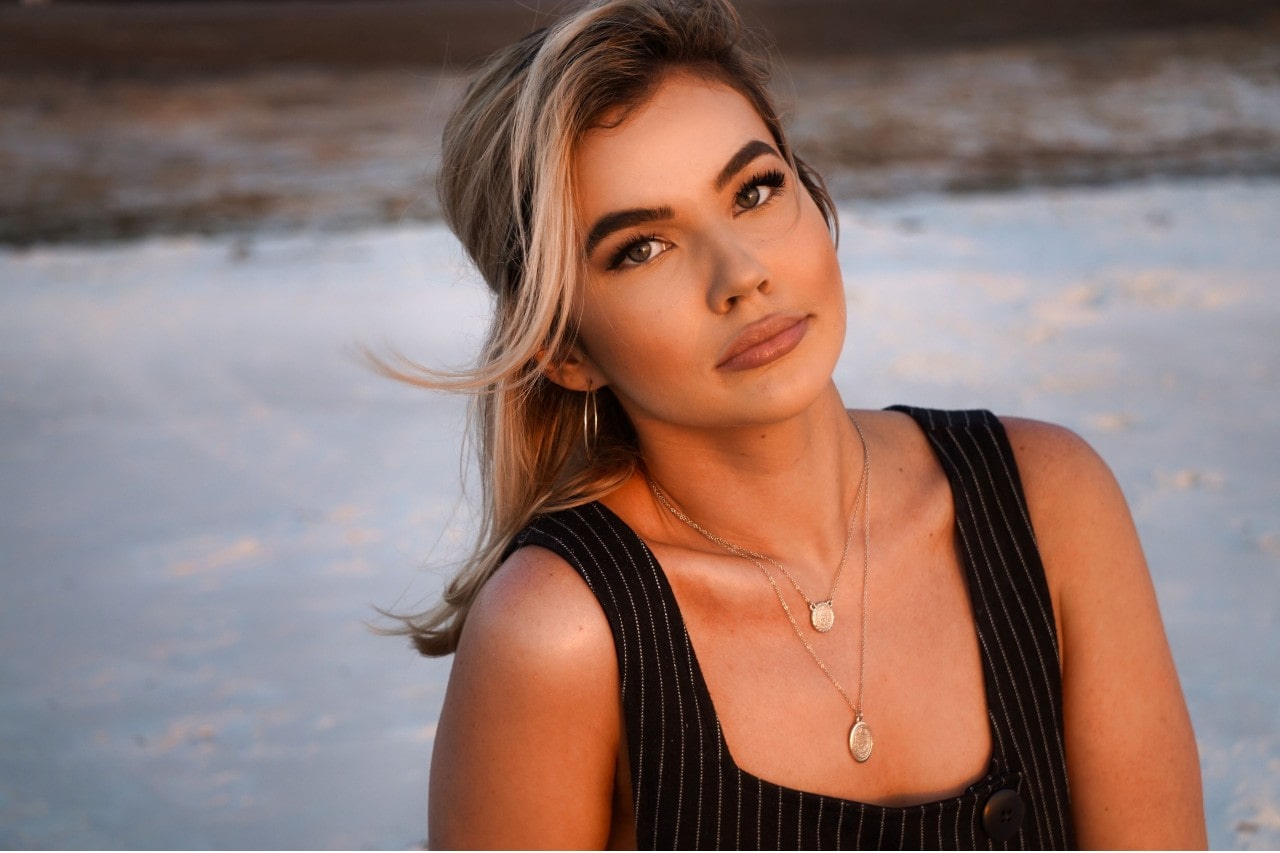 a woman on the beach wearing two layered gold necklaces with circle pendants