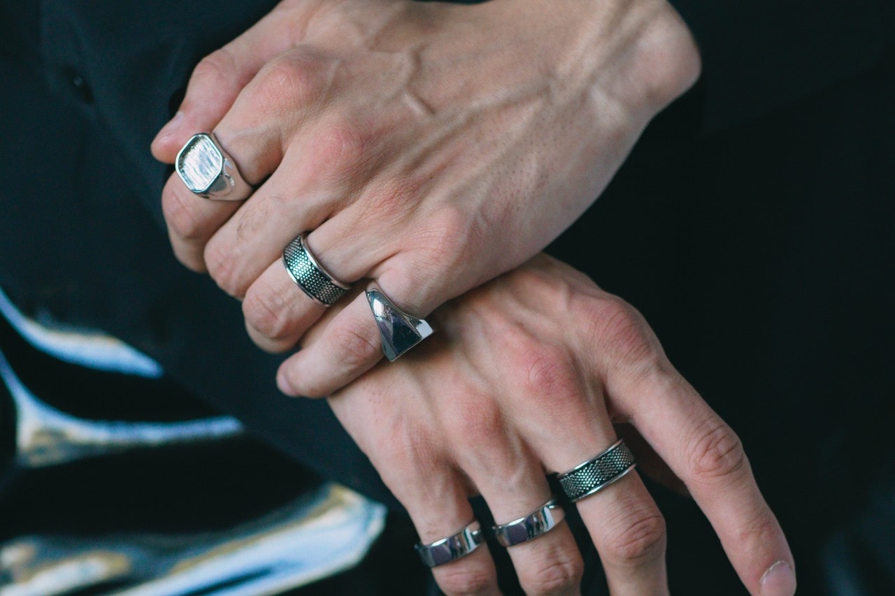 a man’s hands adorned with multiple silver fashion rings