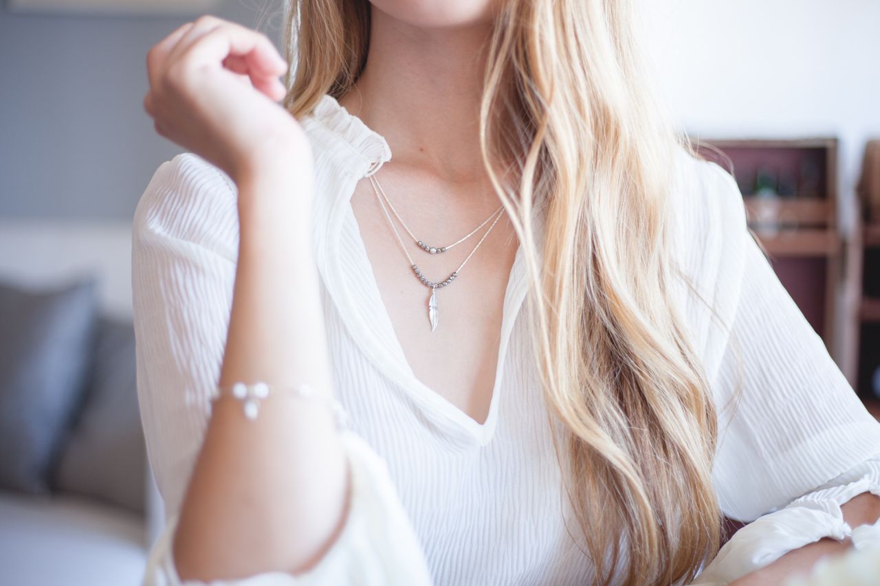 close up image of a woman wearing a white blouse and thin layered necklaces