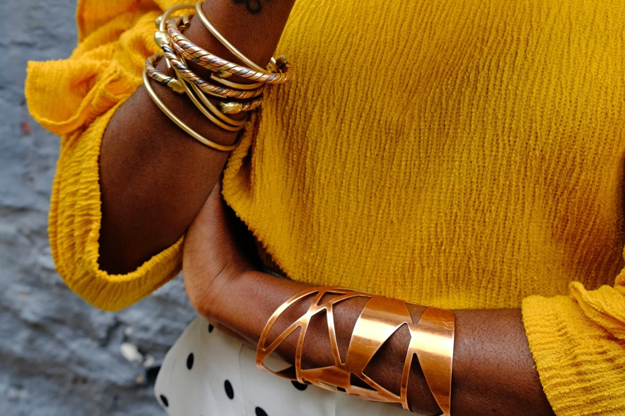close up image of a woman’s wrist donning multiple yellow gold bangle bracelets