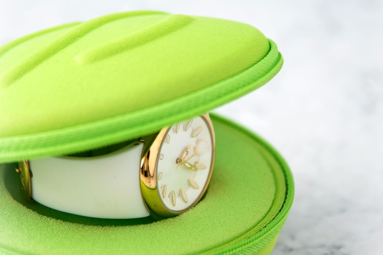 A white and gold watch in a lime green clamshell case.
