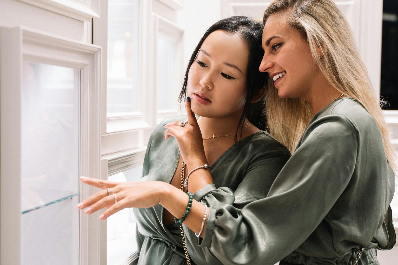 Two women in matching green outfits admire jewelry in a display case.
