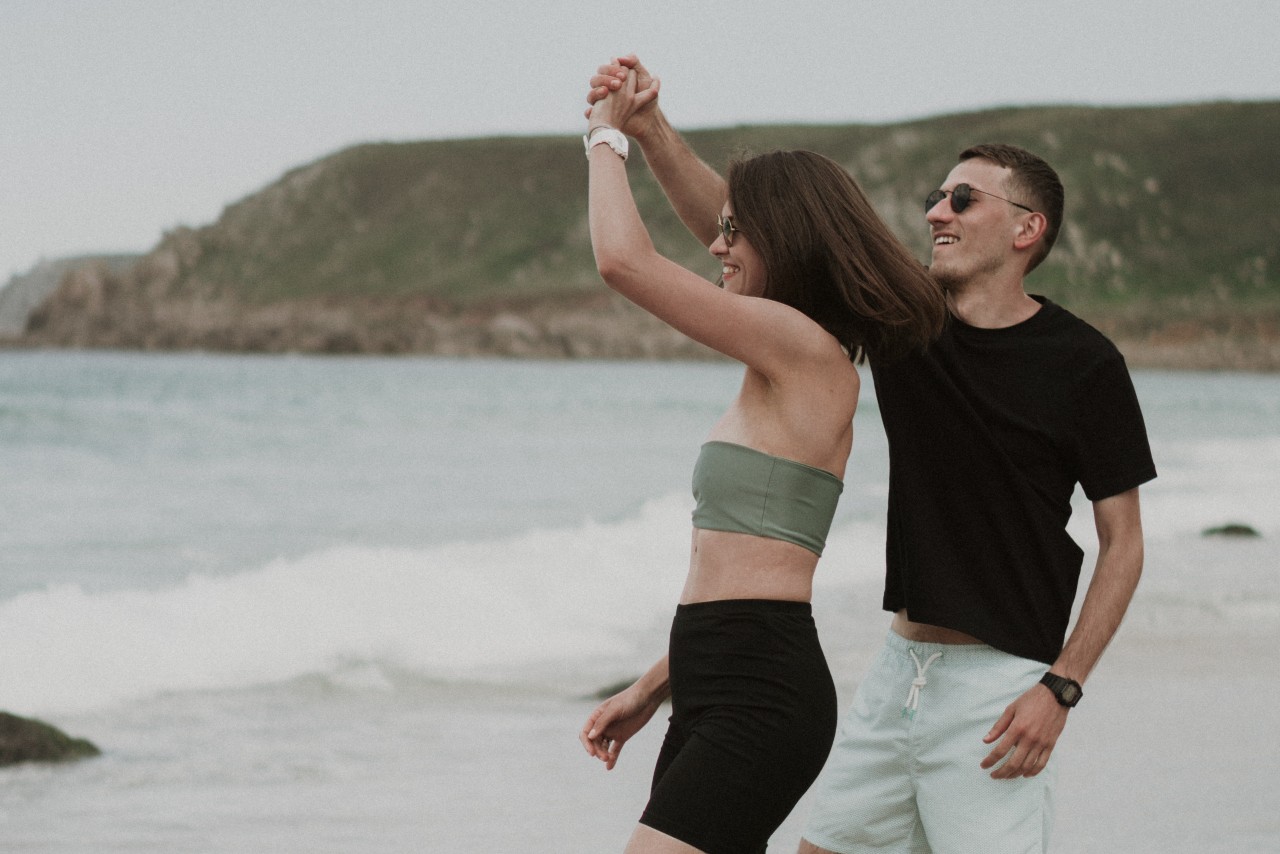 a man and a woman wearing watches and dancing near the ocean