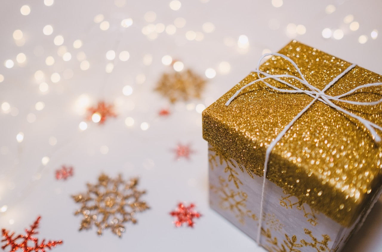 A close up of a glittery gift box against a background filled with christmas light and glittery snowflakes.