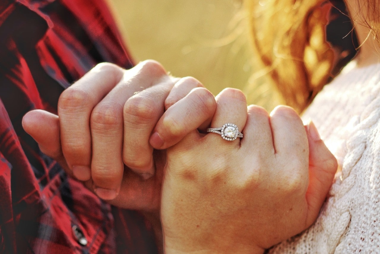 a couple crossing pinkies – the woman wearing a silver engagement ring