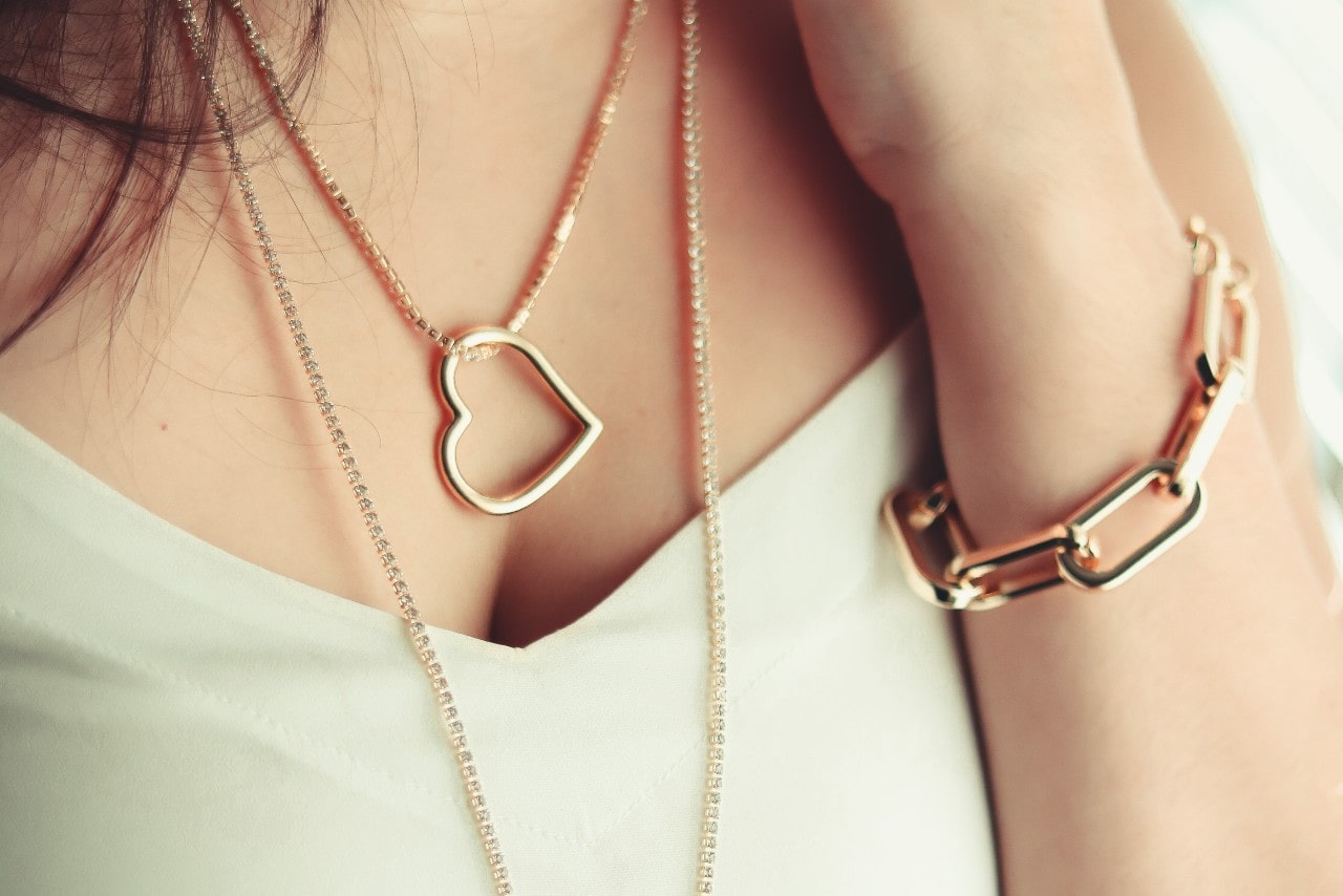 a woman wearing a gold heart necklace and chunky chain bracelet
