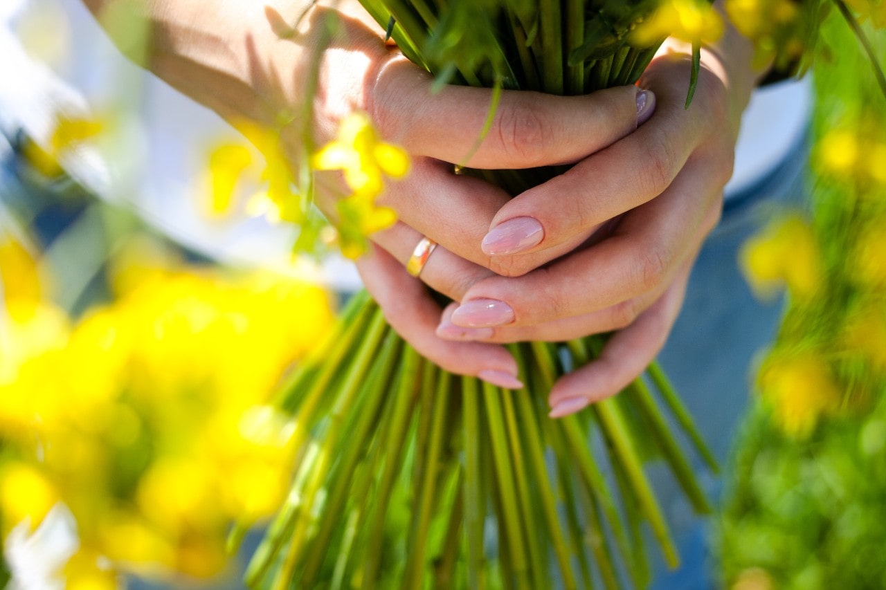 Focus on a bride holding a bouquet of flowers with the focus on her nails and yellow gold wedding band