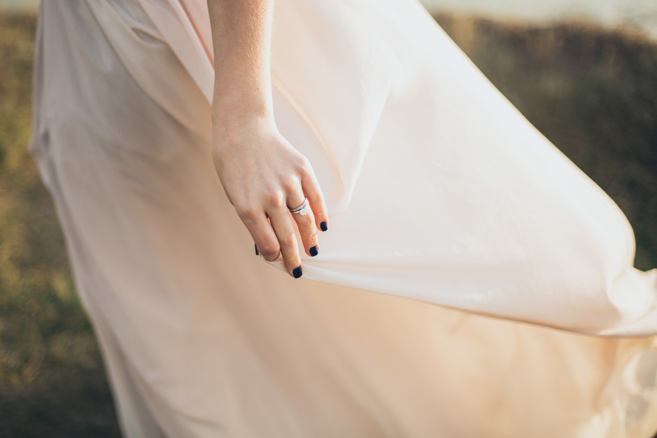A woman gently holding the skirt of her wedding gown with her engagement ring and wedding band the center of focus
