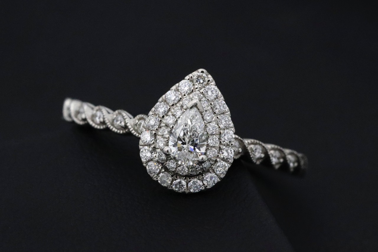 A pear-shaped diamond ring with a double halo of smaller diamonds rests on a dark surface A pear-shaped diamond ring with a double halo of smaller diamonds rests on a dark surface