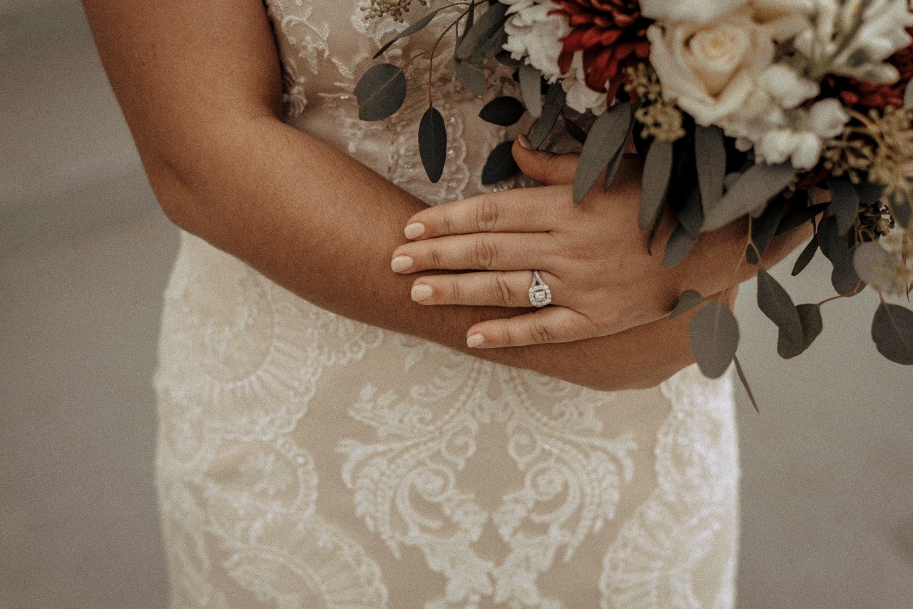 A bride in a white dress is holding a bouquet, showcasing her halo engagement ring. A bride in a white dress is holding a bouquet, showcasing her halo engagement ring.