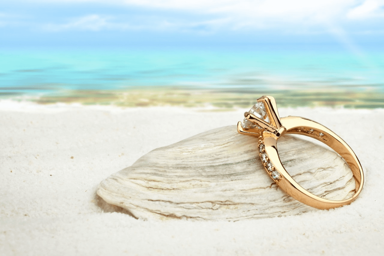 yellow gold diamond engagement ring sitting on a beach.