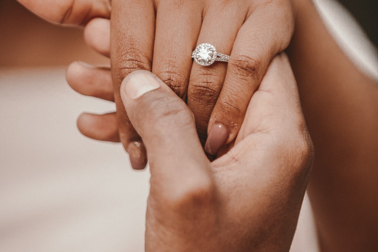 a man holds his partner’s hand, which shows off a halo engagement ring.