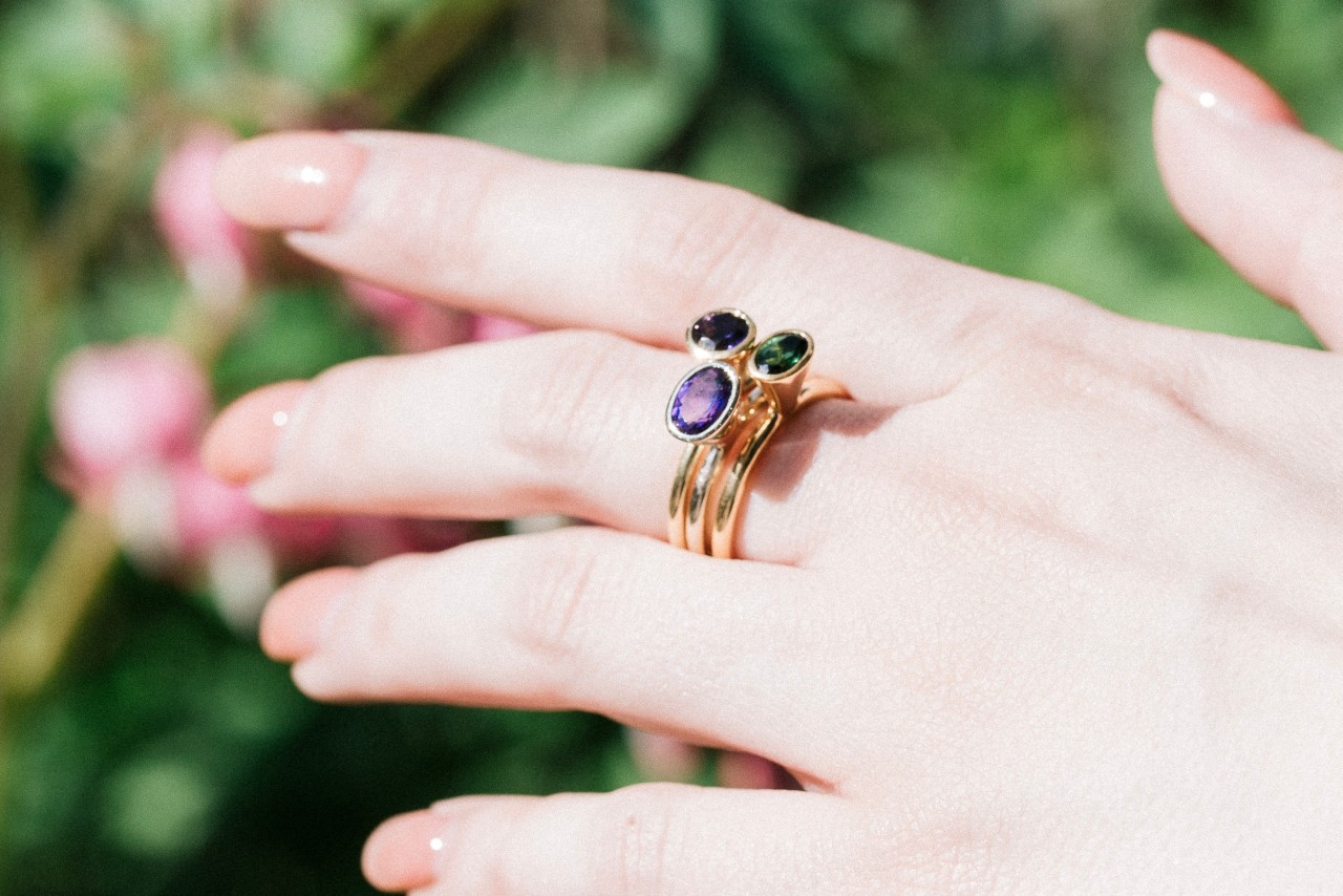 close up image of an outstretched hand wearing three gemstone rings stacked on one finger
