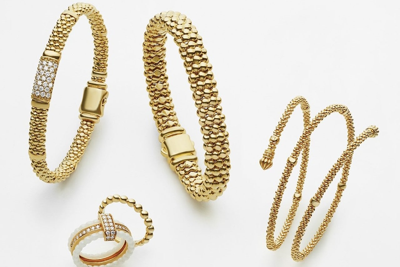 A close up of gold beaded jewelry set featuring textured bangles and two rings on a white surface.