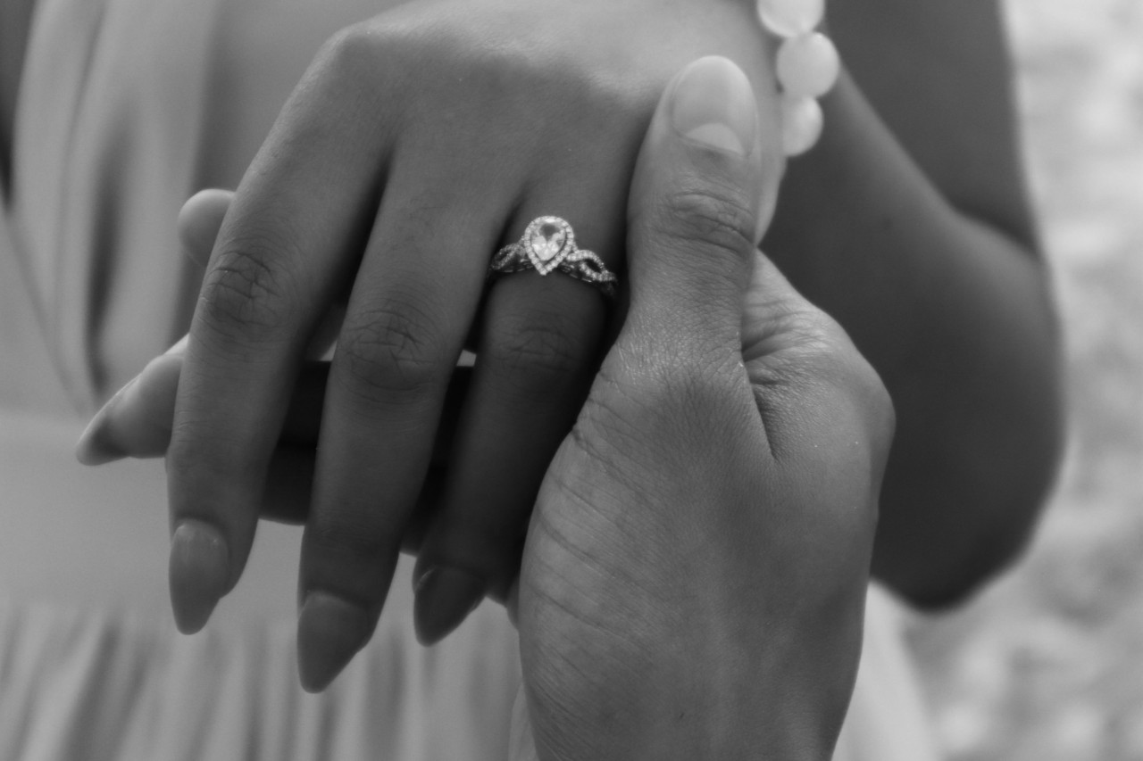 black and white photo of a man holding his brides hand, which is adorned with a pear shape engagement ring