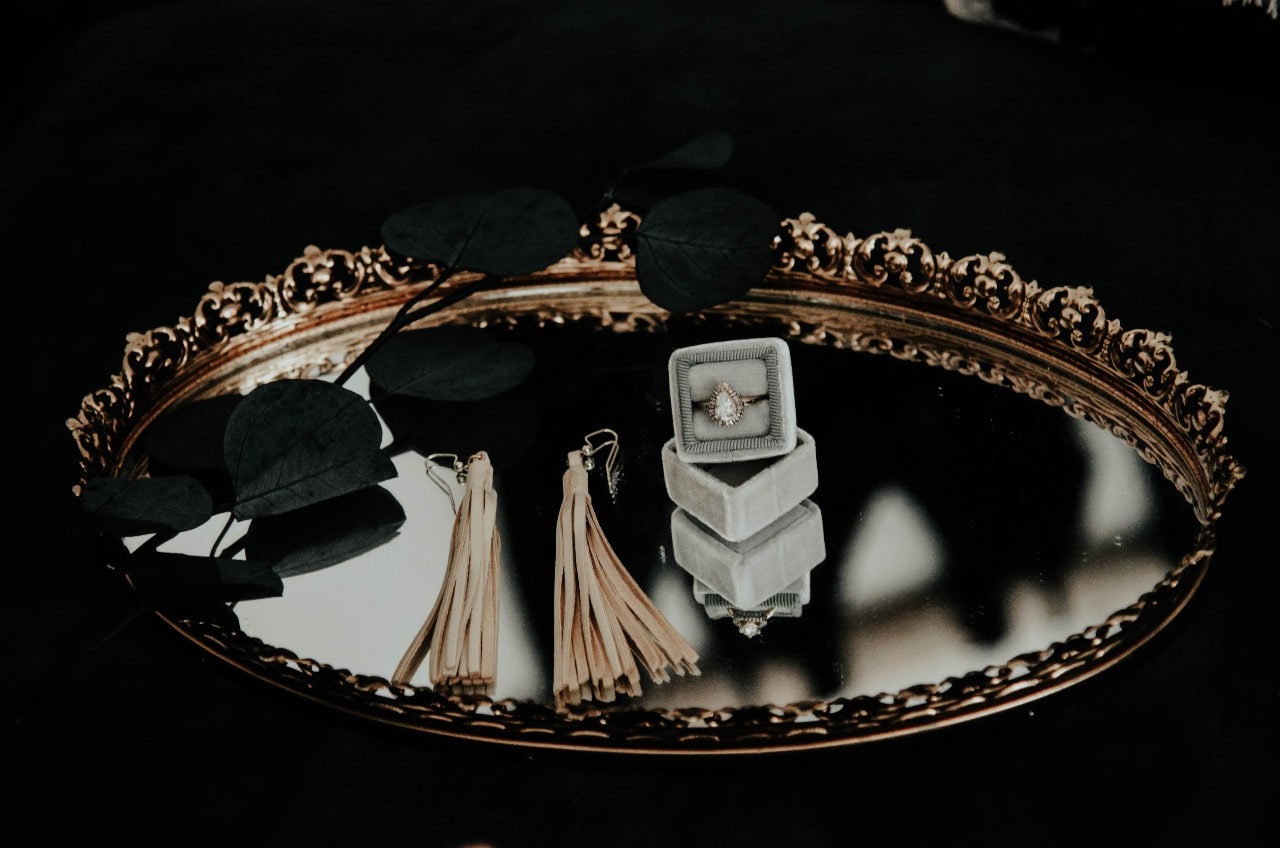 a pair of earrings and a pear shape engagement ring in a box lying on a mirror