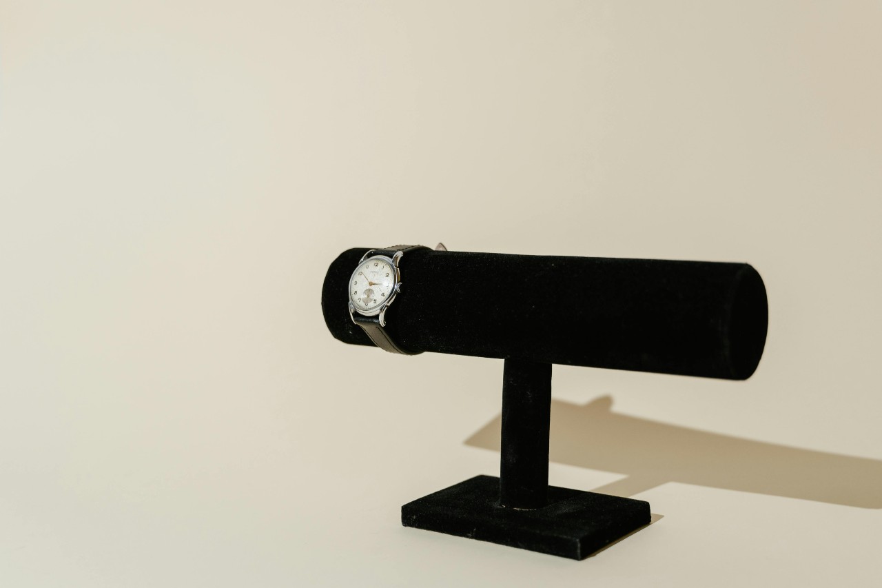 a white and silver watch on a black watch stand against a beige background a white and silver watch on a black watch stand against a beige background