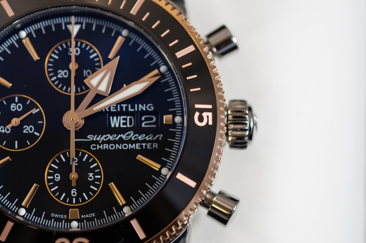 A detailed close-up of a Breitling Superocean Chronometer watch, highlighting its rose gold accents, black dial, and day-date display. A detailed close-up of a Breitling Superocean Chronometer watch, highlighting its rose gold accents, black dial, and day-date display.