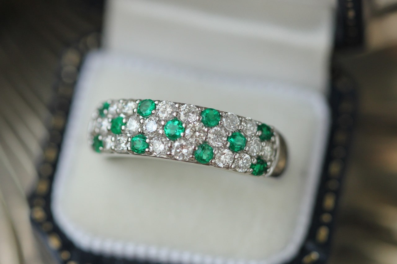 a white gold wedding band featuring pave set diamonds and emeralds in a ring box