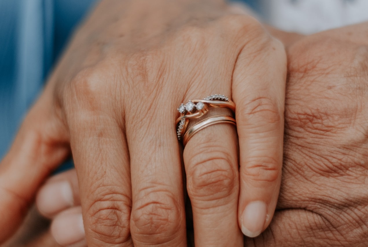 a pair of hands holding, the woman’s hand donning a three stone engagement ring and wedding band