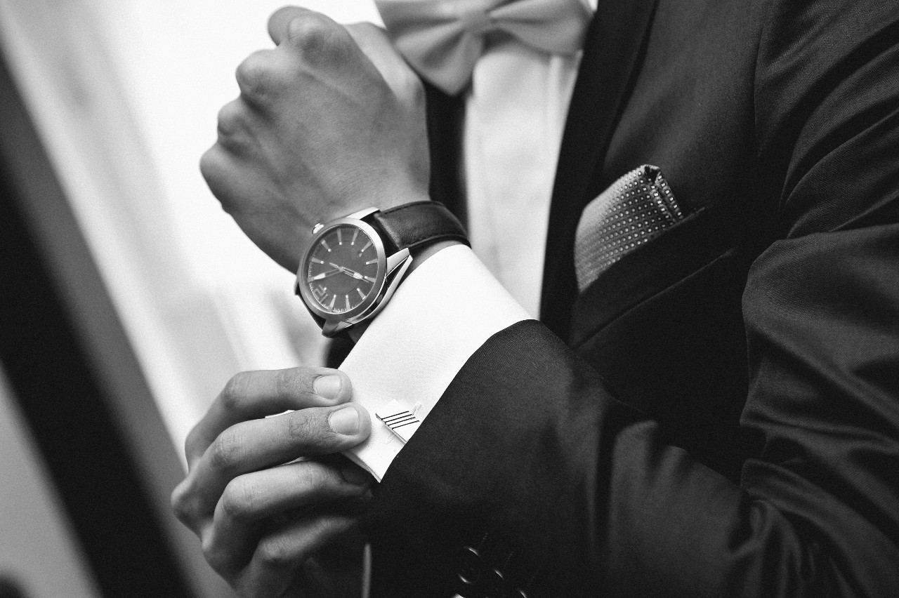 A black and white photo of a man in a suit fixing his cufflinks, showcasing black leather wristwatch. A black and white photo of a man in a suit fixing his cufflinks, showcasing black leather wristwatch.