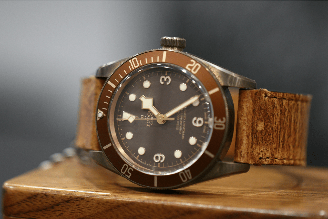 A close up of a TUDOR wristwatch with leather band resting on a wooden surface. A close up of a TUDOR wristwatch with leather band resting on a wooden surface.