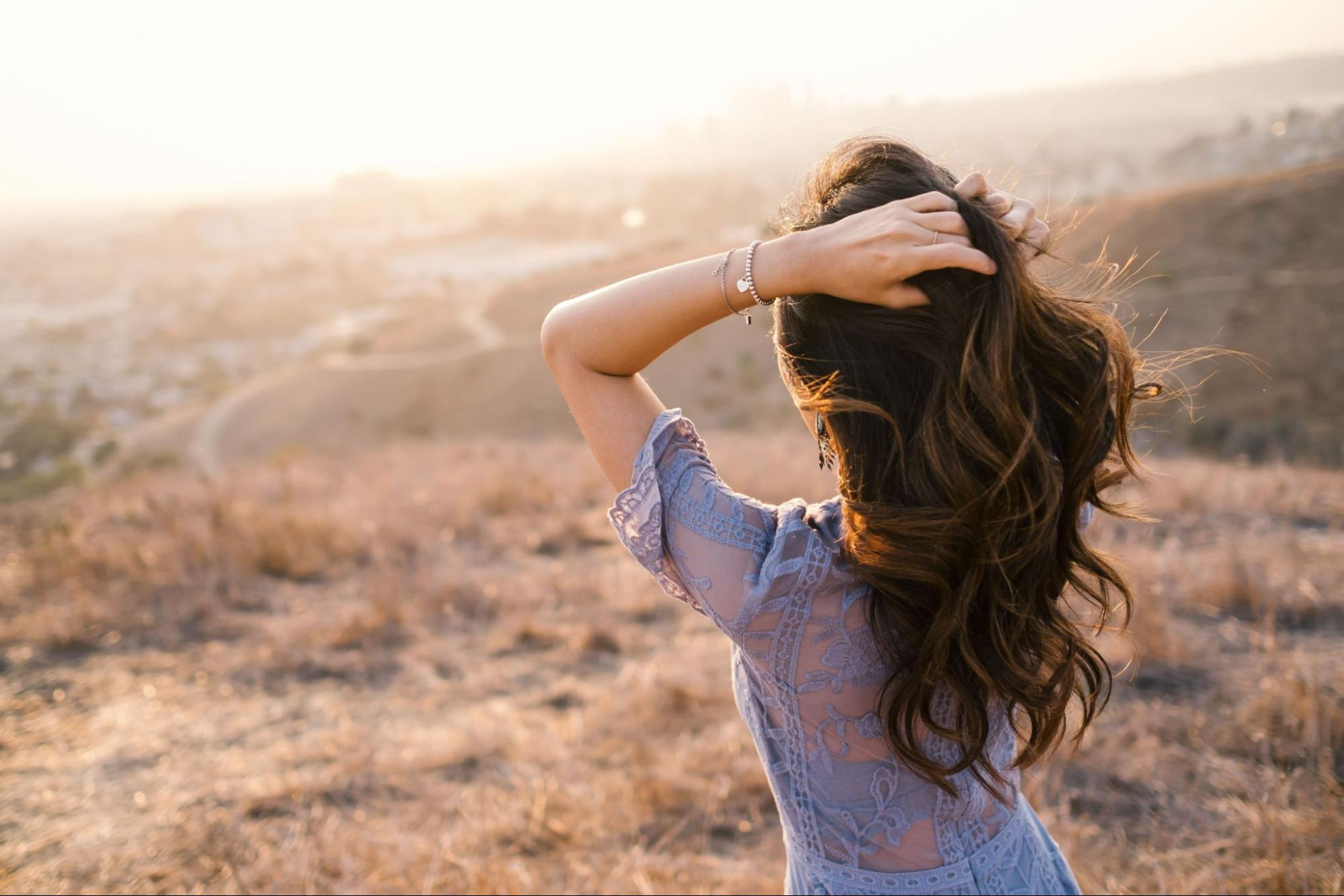 A woman walking in a field ruffles her hair while sporting two thin bangles.