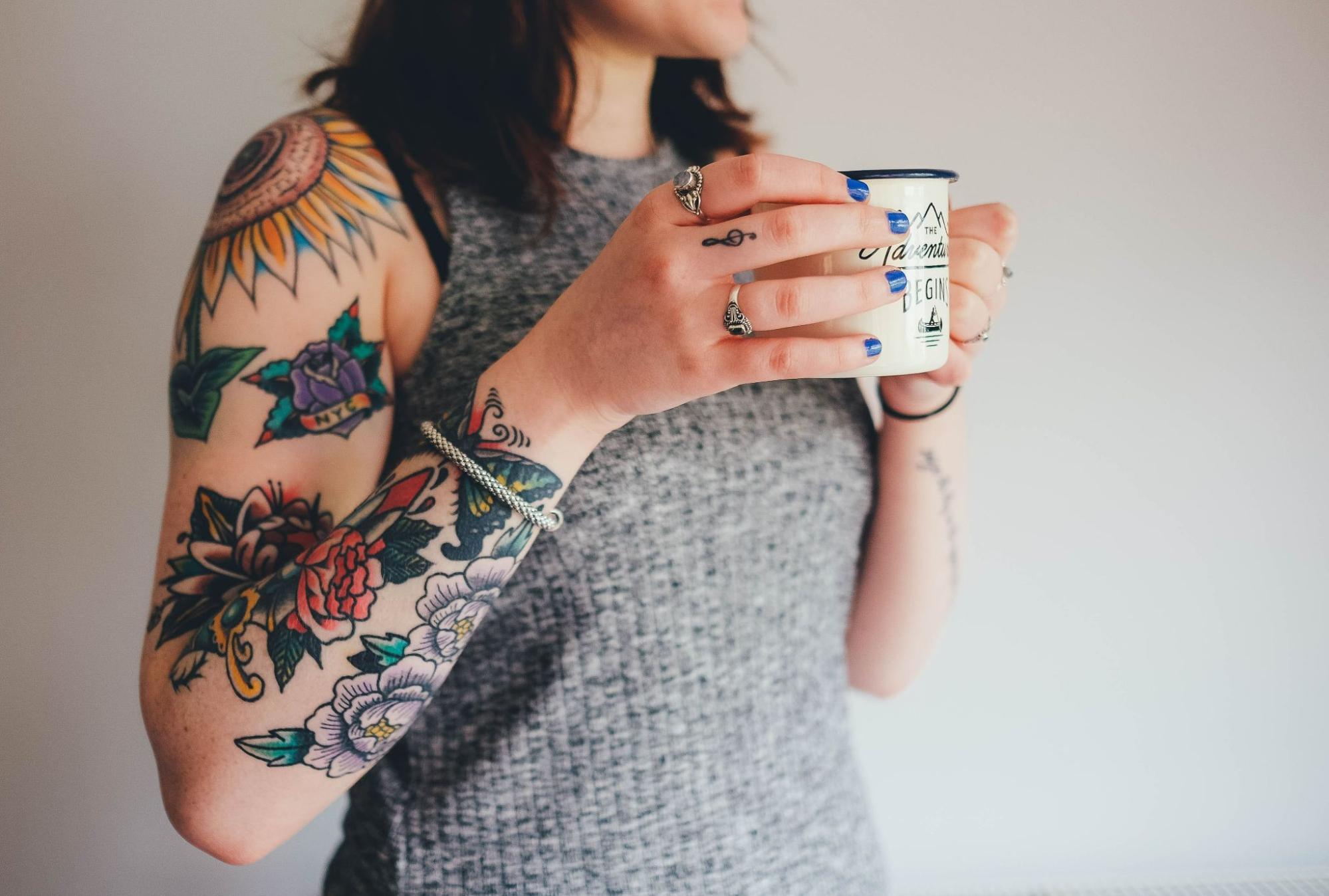 A tattooed woman casually sipping coffee wears a silver bangle and rings.