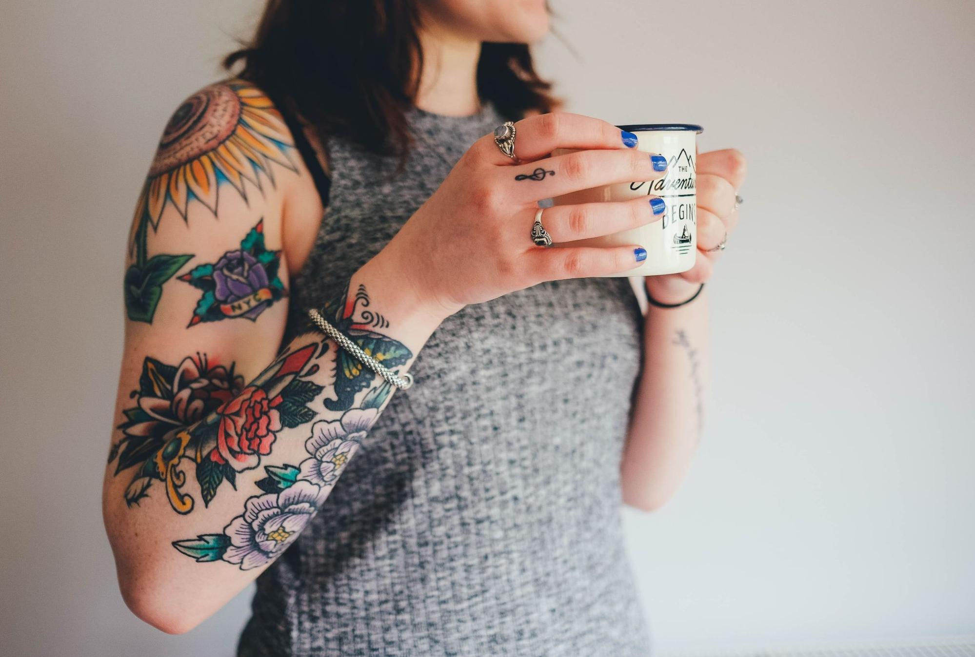 A tattooed woman casually sipping coffee wears a silver bangle and rings. A tattooed woman casually sipping coffee wears a silver bangle and rings.