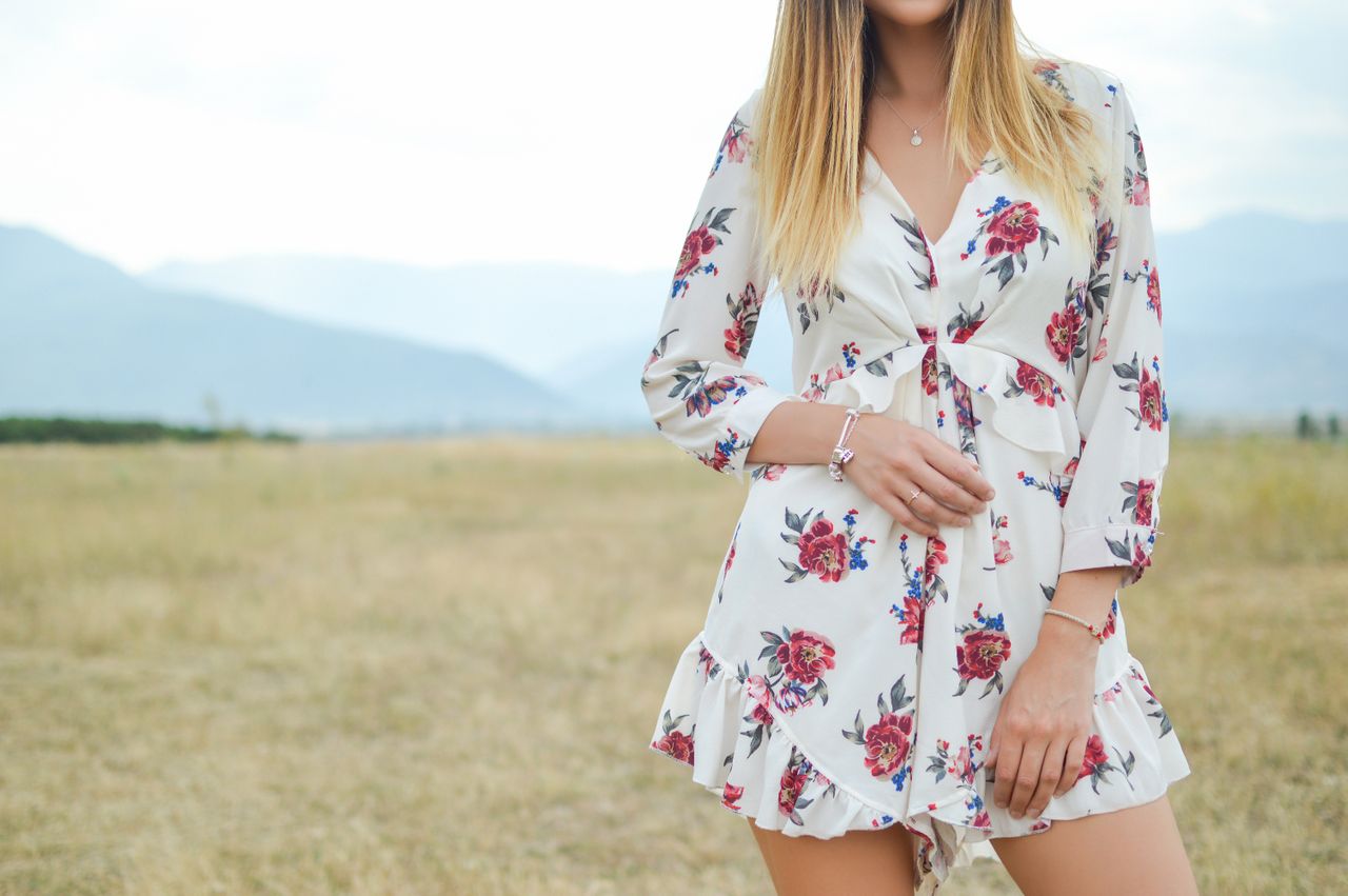 A woman in a floral romper sports two white gold bracelets in a field.
