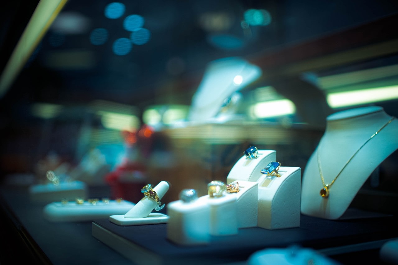 A jewelry store display featuring an array of gold rings with colorful gemstones and a gold necklace A jewelry store display featuring an array of gold rings with colorful gemstones and a gold necklace