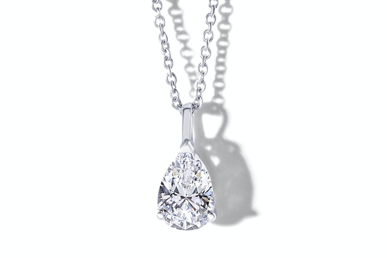 A pear shaped diamond pendant on a silver chain against a white background A pear shaped diamond pendant on a silver chain against a white background